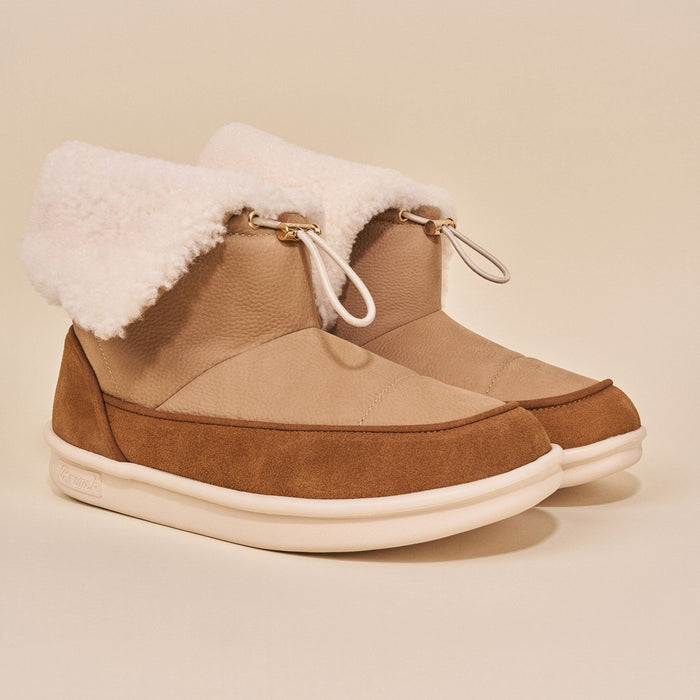 Three-quarter view of Apres Boot in camel nubuck with fold-over shearling cuff, drawcord, suede trim, white sole on beige