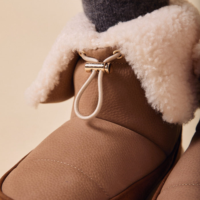Close-up of Apres Boot showcasing folded shearling cuff, gold cord toggle, and camel nubuck texture on neutral background
