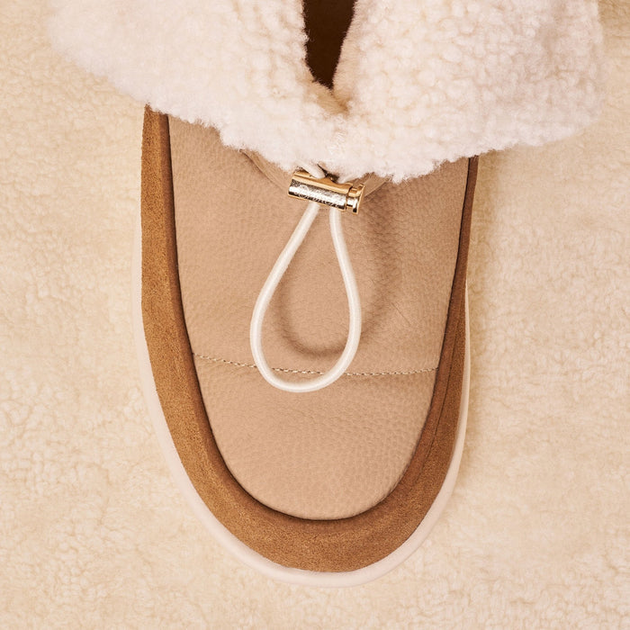Top view of Apres Boot in camel nubuck showing folded shearling cuff, gold toggle, suede trim on cream sherpa background