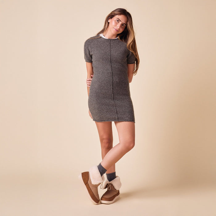 Model standing with crossed legs wearing camel nubuck Apres boots with folded shearling cuff and platform sole on beige background