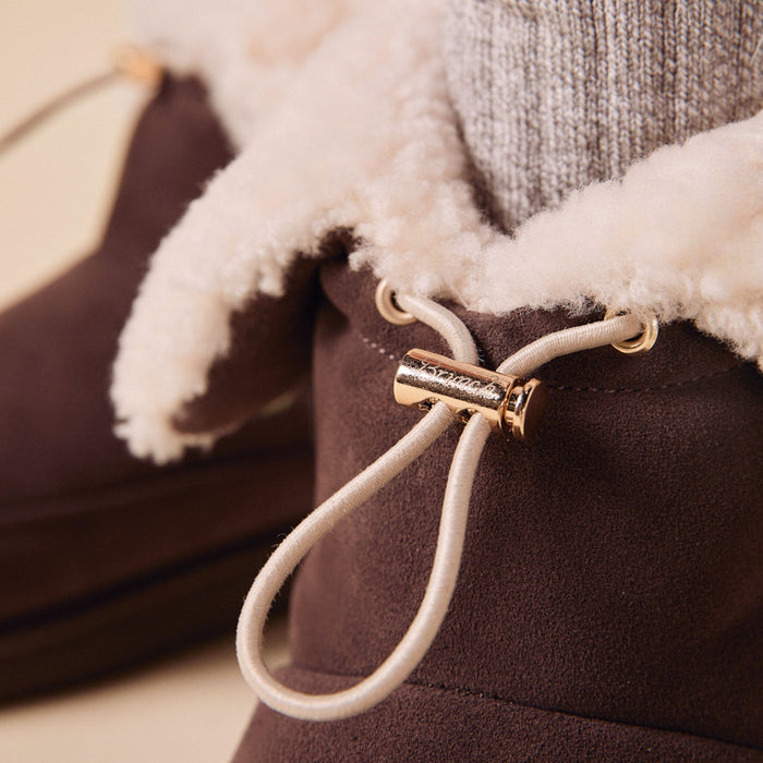 Close-up of Apres Boot showing cream shearling lining and gold-tone cord toggle on dark brown suede