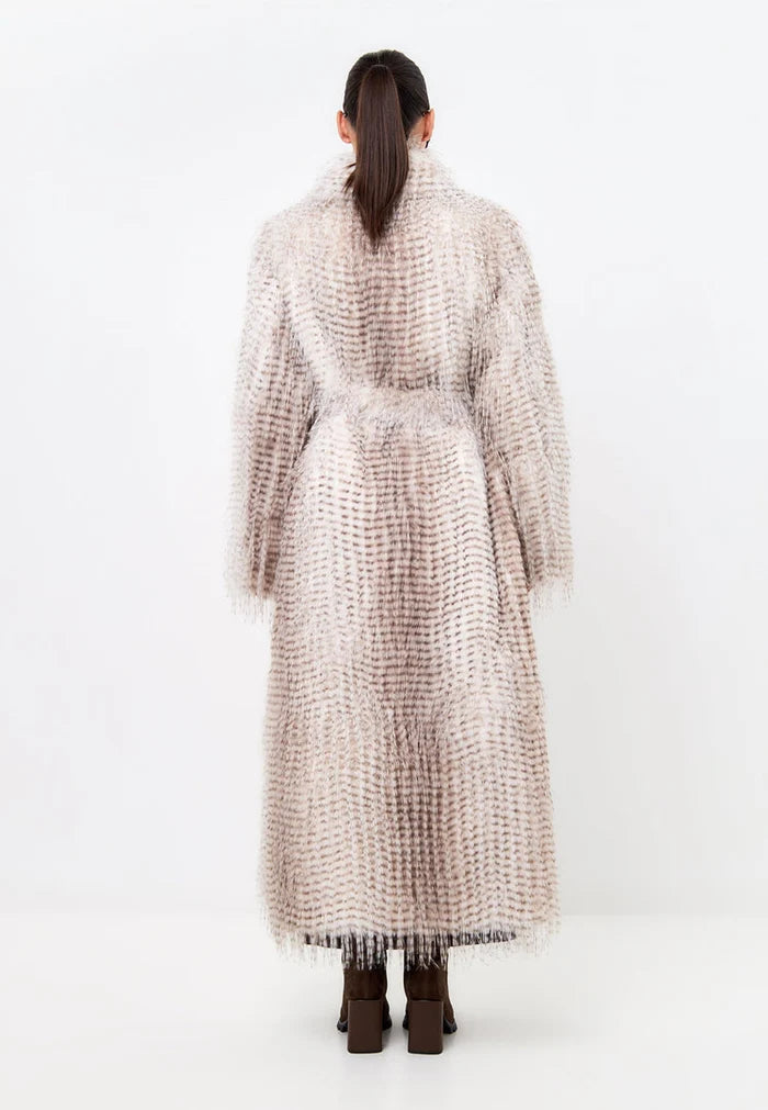 A stylish woman wearing a fashion-forward winter fur coat with a belted design and long faux fur material.