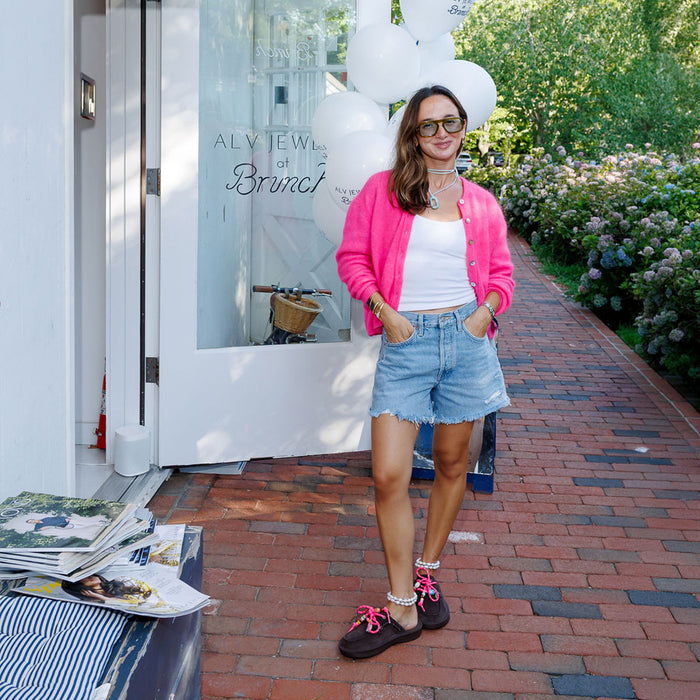 Woman standing outside ALV JEWELS at Brunch, wearing pink cardigan, brown suede shoes laced with hot pink paracord