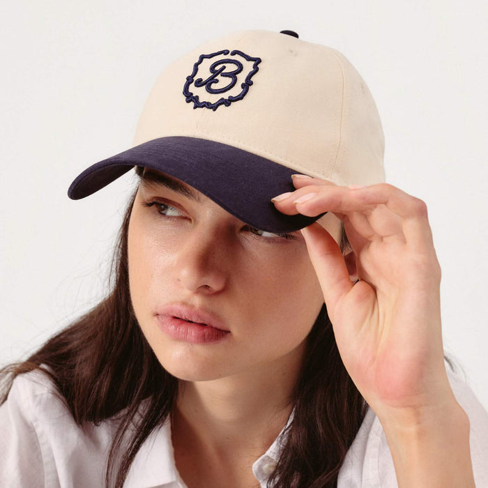 Three-quarter front of Retro Crest Cap in cream with navy brim showing embroidered crest on model, white background
