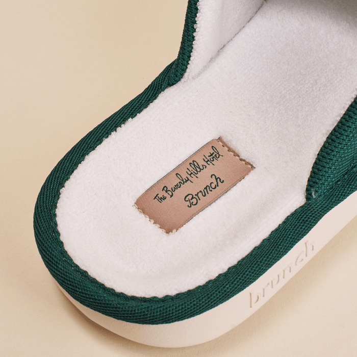 Close-up of Essential Beverly Hills Hotel slipper insole showing white terry lining, pink label reading The Beverly Hills Hotel Brunch and green knit trim