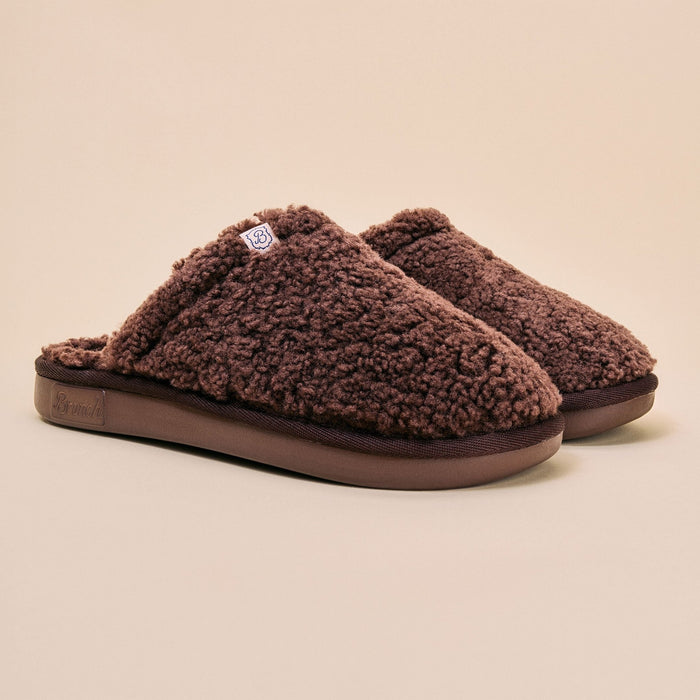 Three-quarter view of Essential All Shearling slipper showcasing plush brown shearling and slip-on mule design on a neutral beige background