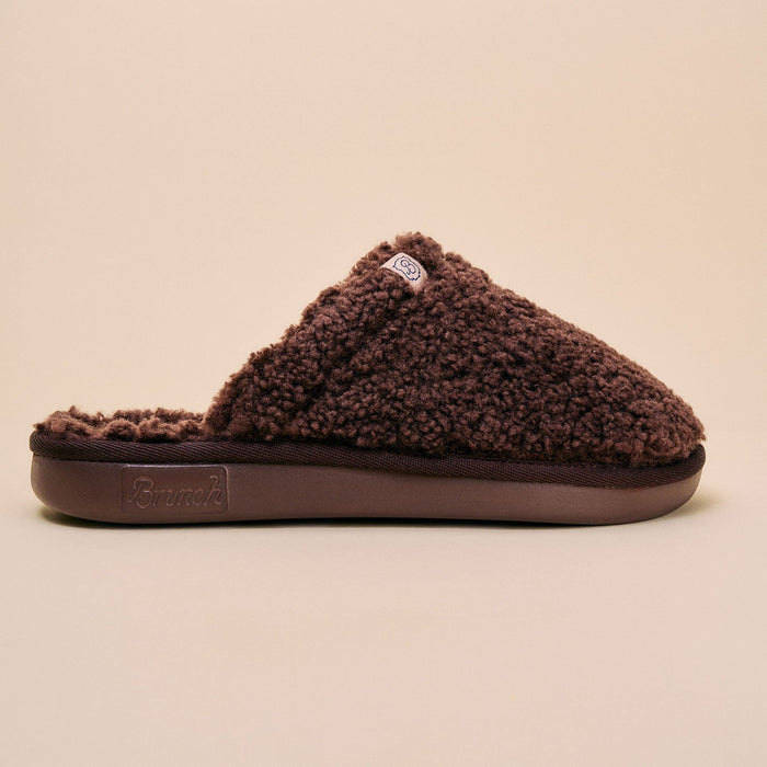 Side view of brown Essential All Shearling slipper showing plush shearling upper and slip-on mule on beige background