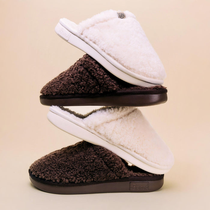 Side view of stacked Essential All Shearling slippers showing plush natural shearling upper and cushioned EVA sole on a light beige background