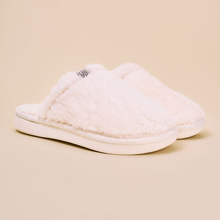 Angled view of Essential All Shearling slipper showing plush natural shearling upper and cushioned white EVA sole on beige