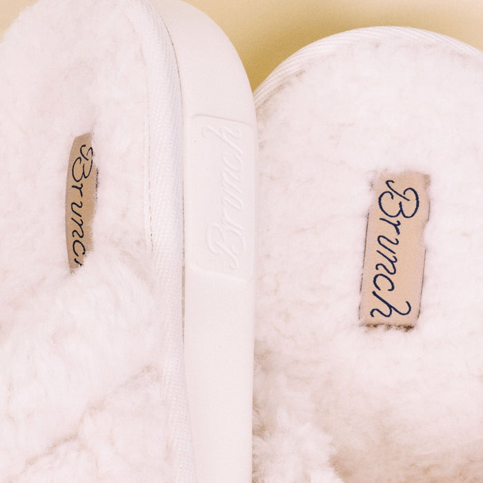 Close-up of Essential All Shearling slipper showing natural shearling lining, Brunch logo tag and white sole edge