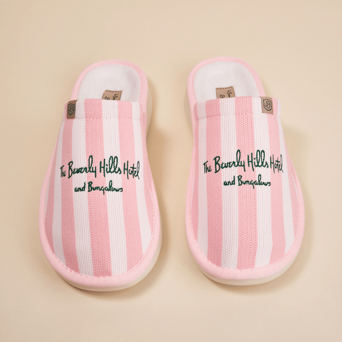 Overhead view of pink striped Essential slippers with embroidered Beverly Hills Hotel text and plush lining on beige background