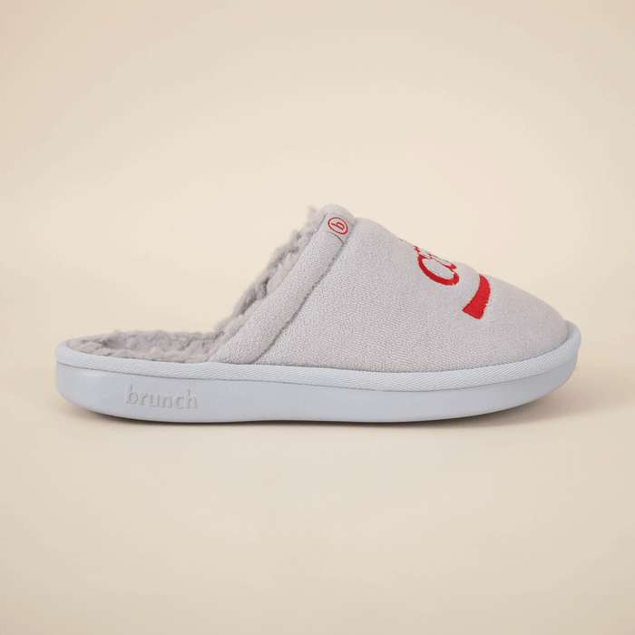 Side view of grey Brunch x Diet Coke shearling slipper showing faux-shearling lining and embroidered red Coke logo on beige background