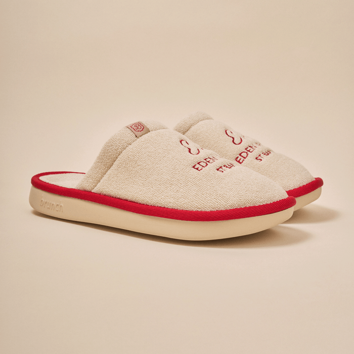 Three-quarter view of beige Essential Eden Rock slipper with terry upper, red Eden Roc embroidery, red trim and cream EVA sole
