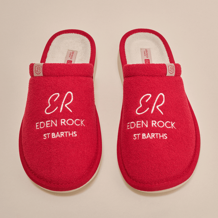 Top-down view of Essential Eden Rock red slip-on slippers showcasing white embroidered text ER EDEN ROCK ST BARTHS on terry uppers with cream background