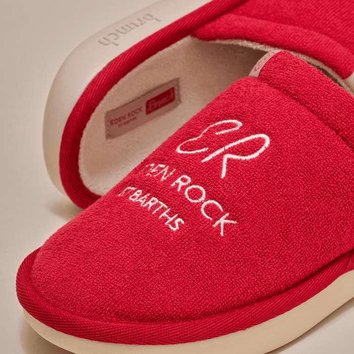 Close-up of Eden Rock slipper showcasing white embroidered EDEN ROCK ST BARTHS on red terry upper with cream outsole on light background