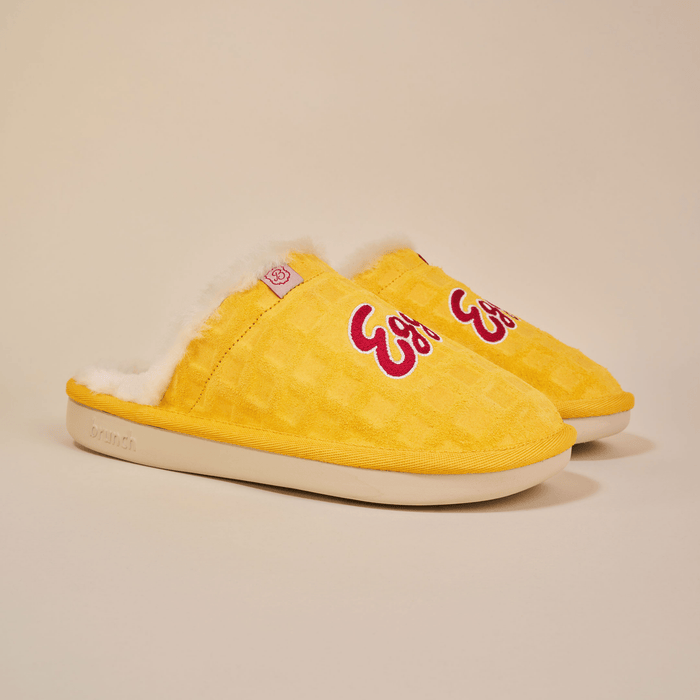 Angled view of yellow Eggo slippers with waffle-suede upper, embroidered logo, shearling lining, and cream outsole