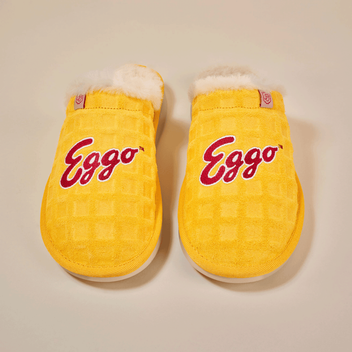 Top-down view of Essential Eggo slippers showing yellow waffle-textured suede, red "Eggo" embroidery, and white shearling lining