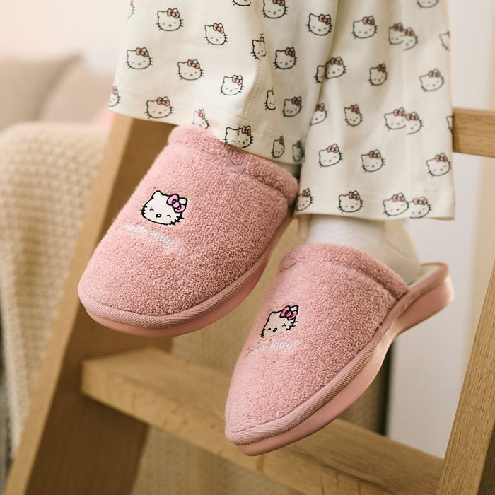 Three quarter view of pink terry Hello Kitty slippers worn by a model showing embroidered Hello Kitty and cushioned pink outsole