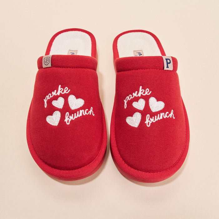 Top view of crimson Essential Parke fleece slippers showing white embroidered parke and brunch text, three hearts, and white lining on beige background