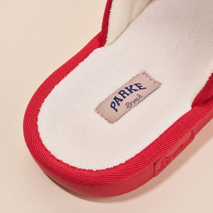 Close-up of Essential Parke slipper in crimson showing fleece terry insole and red trim with Brunch label on pale beige background