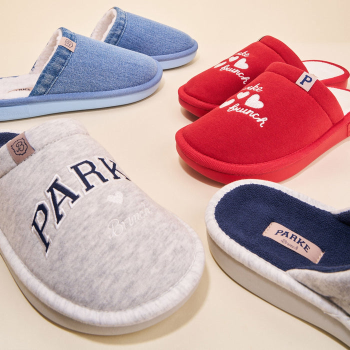 Three-quarter view of Essential Parke crimson fleece slippers with embroidered white hearts and Brunch logo, other color variants on beige background