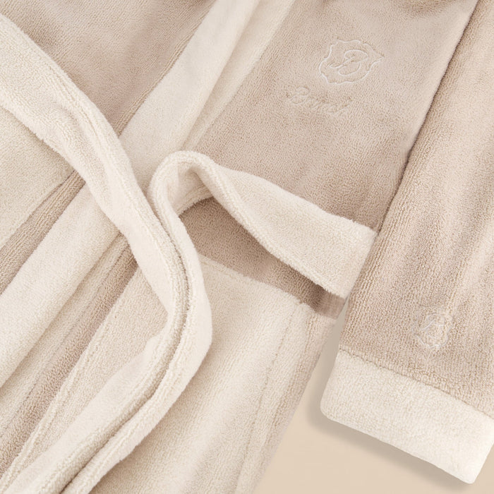 Close-up of beige terry Essential Robe showing plush texture, tied belt, and embroidered logo on a light background