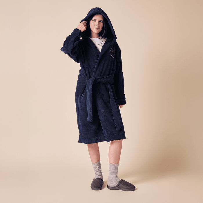 Three-quarter view of navy terry robe on model showing oversized hood, belted waist, front pockets, mid-calf, beige background