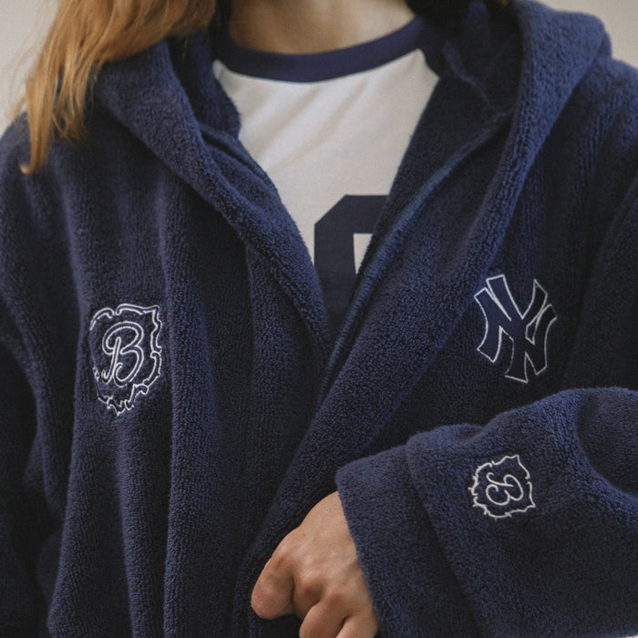Close-up front of navy terry Essential Robe showing hood, embroidered Yankees crest on chest, Brunch crest on chest and cuff, model wearing white ringer tee
