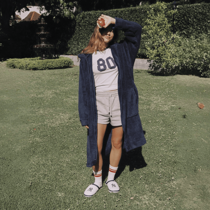Front view of navy Essential Robe on model showcasing hood, pockets, belted oversized fit in a sunlit garden