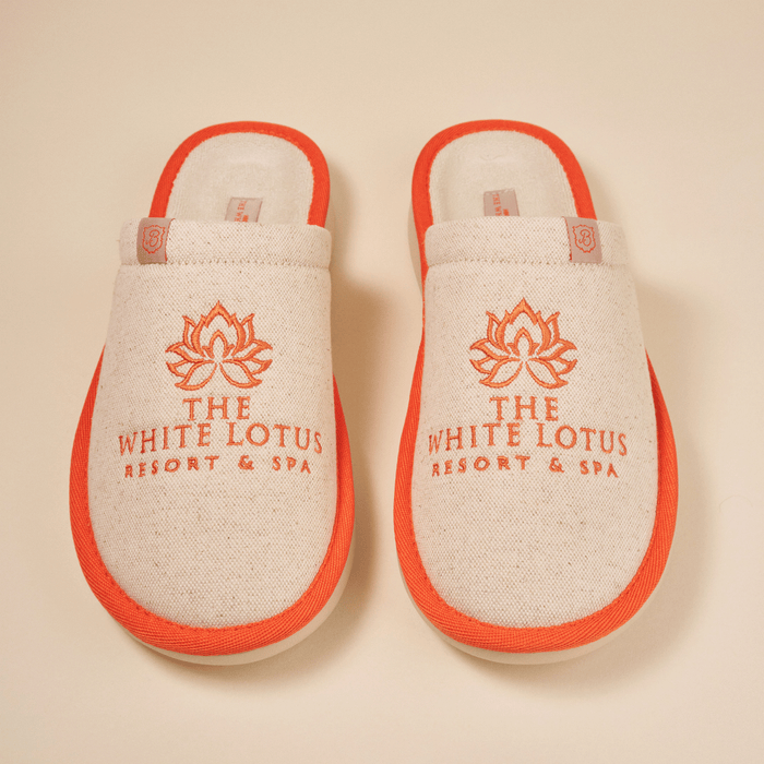 Top-down view of Essential The White Lotus linen slippers in beige with orange trim, embroidered THE WHITE LOTUS RESORT & SPA logo