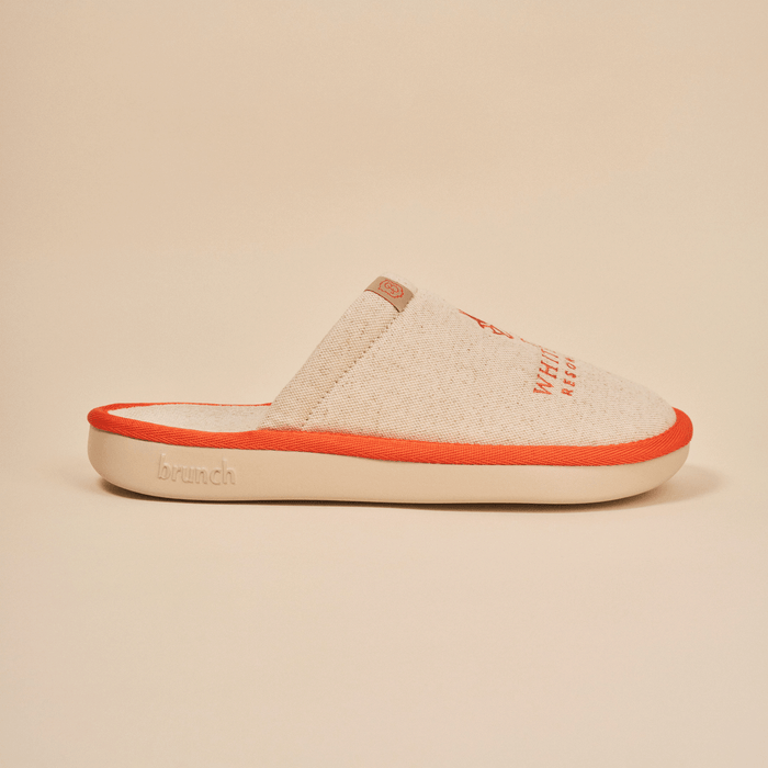 Side view of Essential The White Lotus slipper in beige showcasing linen upper, orange piping, and Brunch embossed EVA sole on neutral background