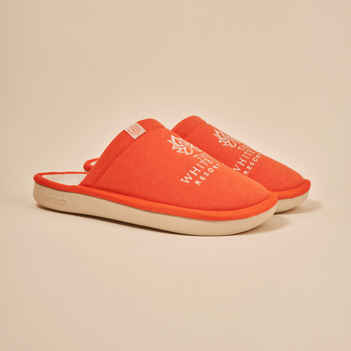 Three-quarter view of orange White Lotus slipper with embroidered White Lotus logo and EVA sole on beige background