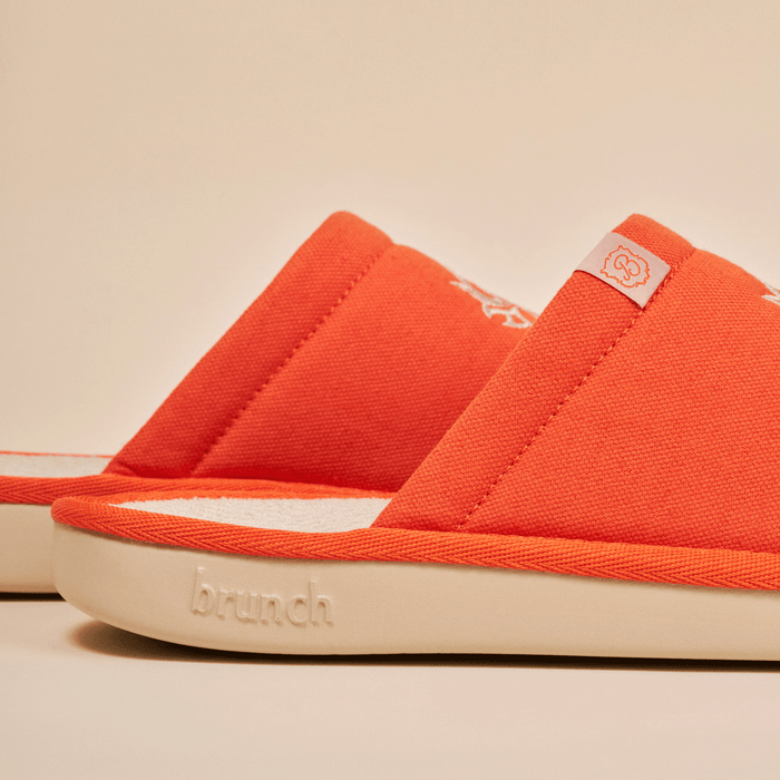 Side close up of White Lotus slipper in orange showing embroidered linen upper and embossed Brunch on cream EVA sole