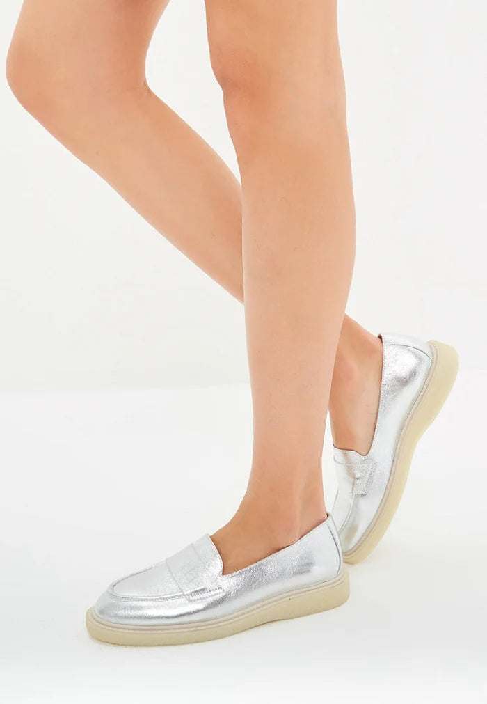 A chic pair of slip-on silver loafers with a flat sole for women, perfect for a stylish outfit.