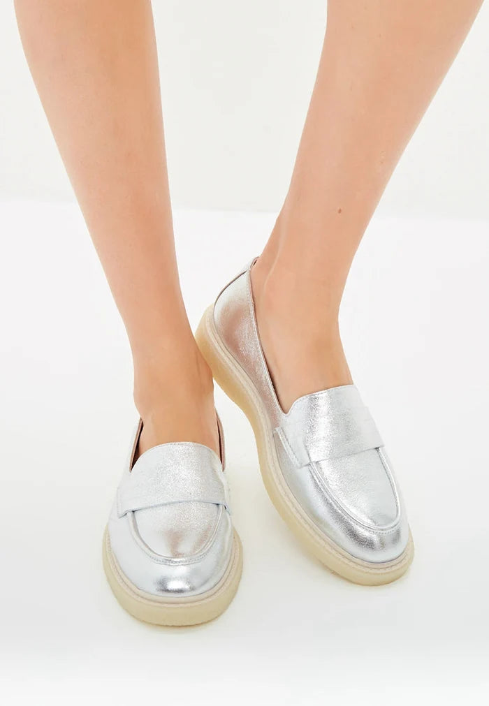 A pair of stylish women's slip-on loafers in silver with a flat sole design.