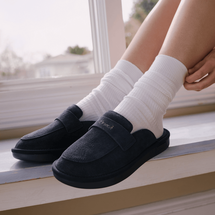 Three-quarter view of Loafer in navy suede showcasing suede upper and embroidered Brunch strap on a windowsill with model wearing white socks