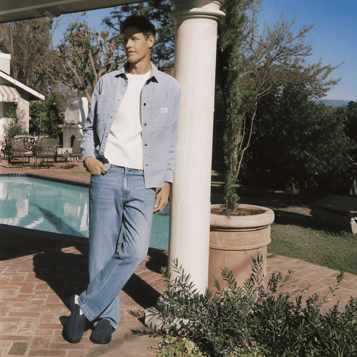 Man wearing navy suede Yankees loafers standing by a poolside patio, leaning against a column