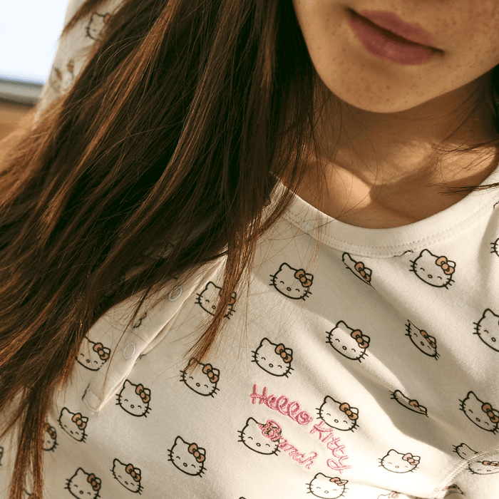 Close-up of cream Hello Kitty pajama top showing pink embroidered Hello Kitty Brunch logo and all-over Hello Kitty head print on a model