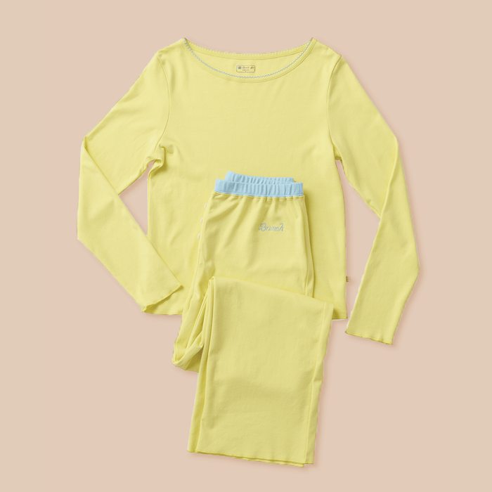 Flat lay of Sunshine Yellow pajama set with picot-trim neckline, blue waistband, and Brunch embroidery on pink background