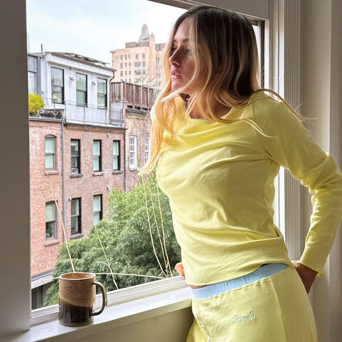 Three-quarter view of Sunshine Yellow PJ set with long-sleeve top and elastic-waist shorts, model leaning at a window