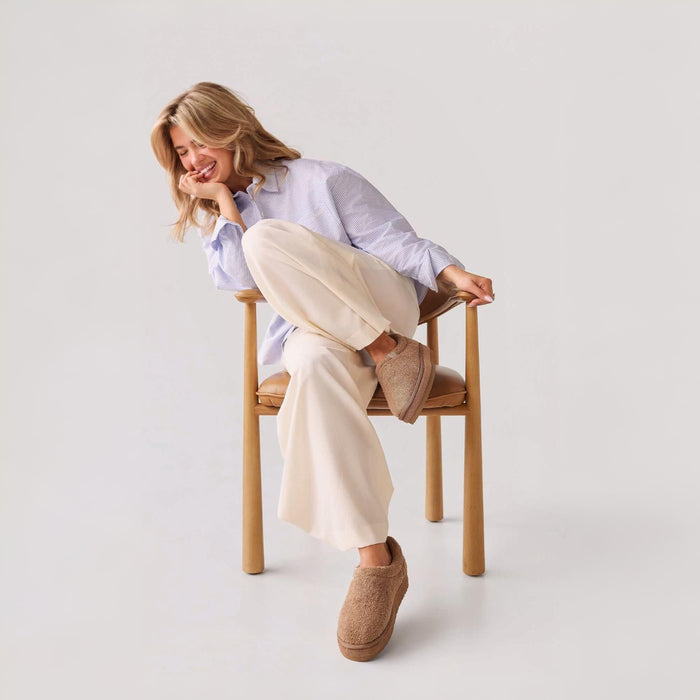 Model seated on wooden chair wearing Dune Puff XXL terry platform slippers in a neutral studio setting