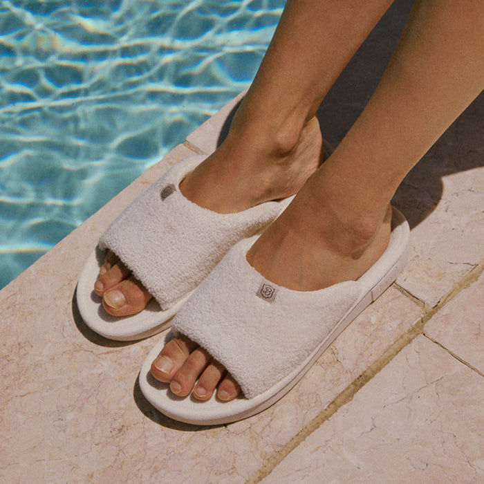 White slippers worn by a person standing by a pool.