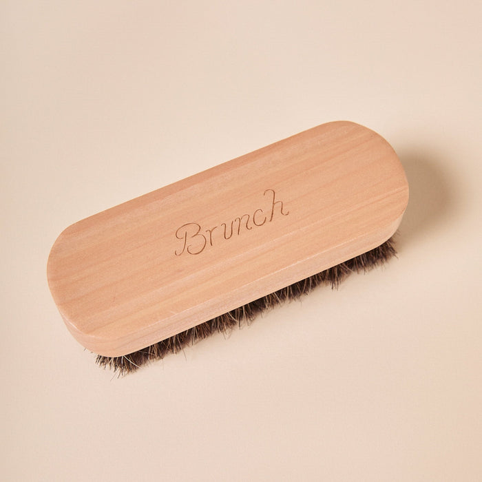 Top view of suede brush showing engraved Brunch wooden handle and dense horsehair bristles on a pale beige background