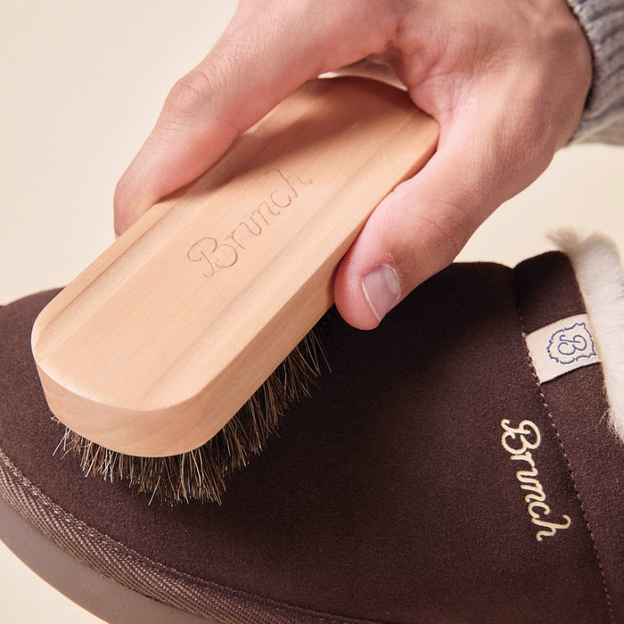 Top-down view of suede brush showcasing wooden Brunch-engraved handle and horsehair bristles brushing a brown suede slipper