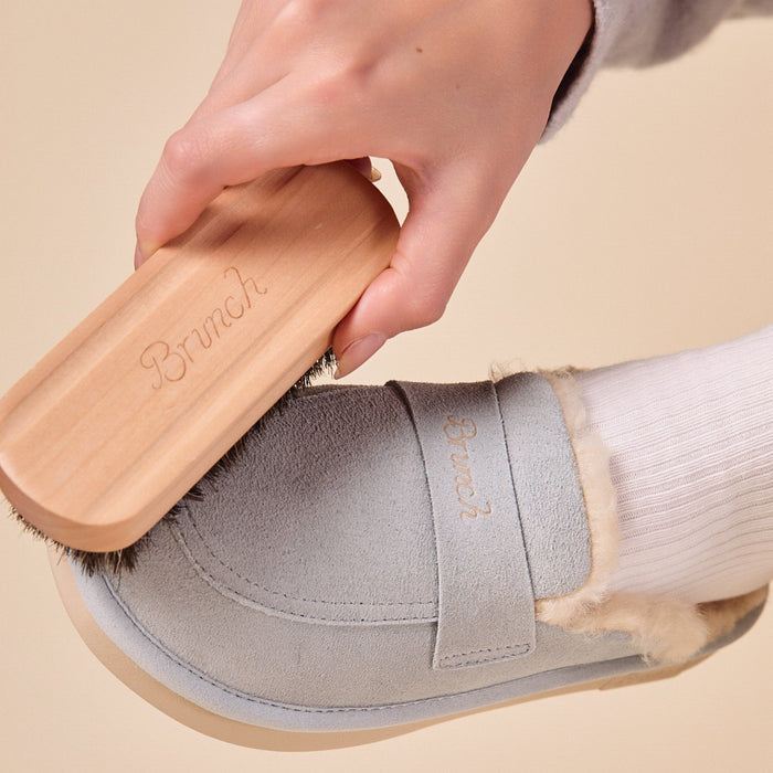 Close-up of suede brush with engraved Brunch wooden handle and horsehair bristles brushing a gray suede slipper